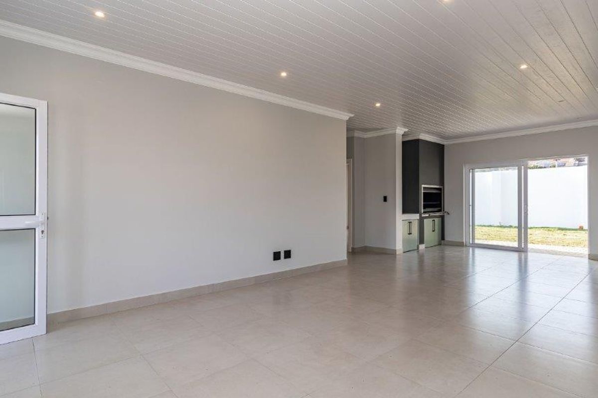 Spacious open-plan living area featuring tiled floors, a tongue and groove ceiling with recessed lighting, and a built-in braai with sliding door access.