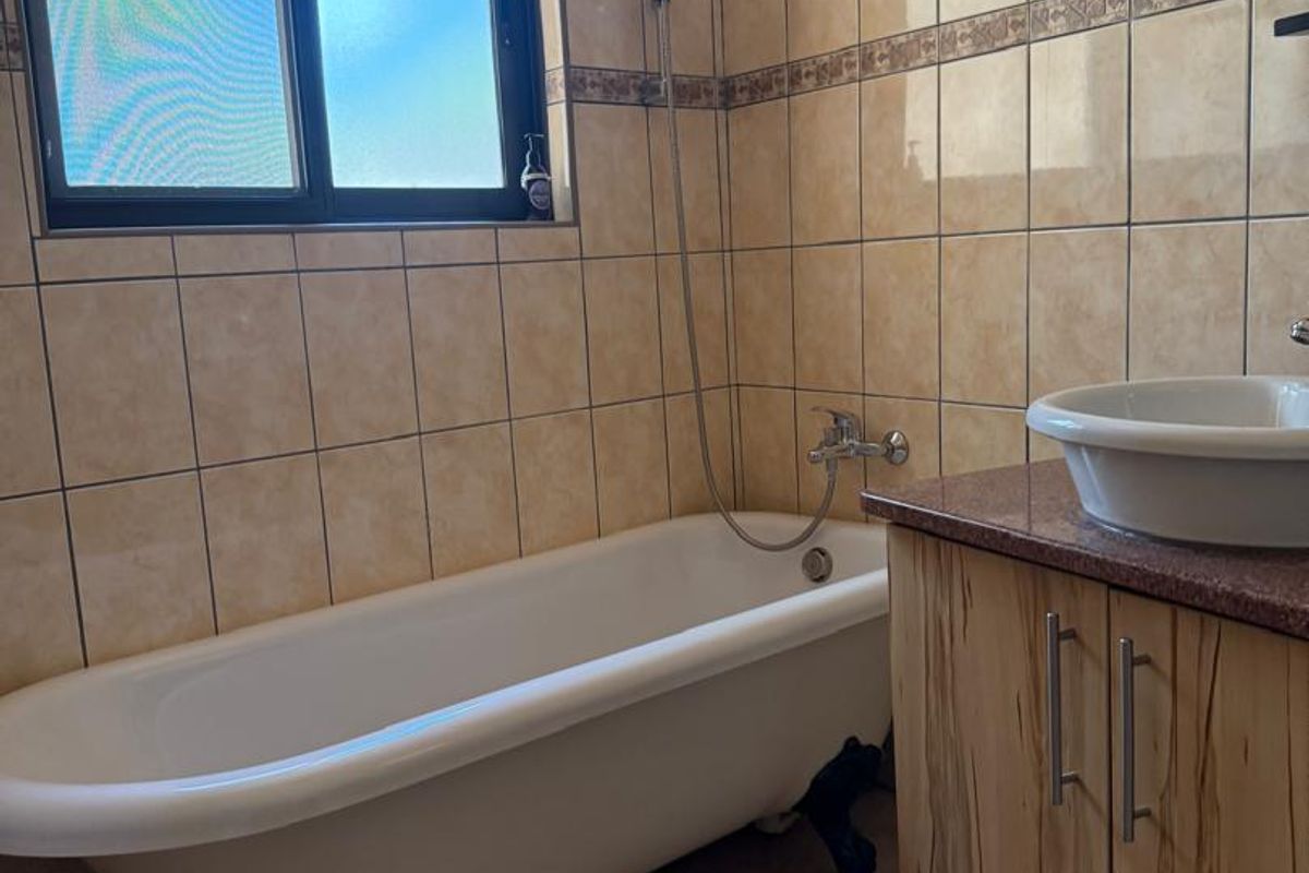 A bathroom featuring a classic clawfoot bathtub, a vanity with a vessel sink, and floor-to-ceiling wall tiling.