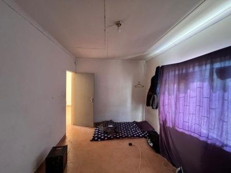 A bedroom featuring tiled flooring and ceiling light fixture, currently showing signs of wear on the walls and ceiling.