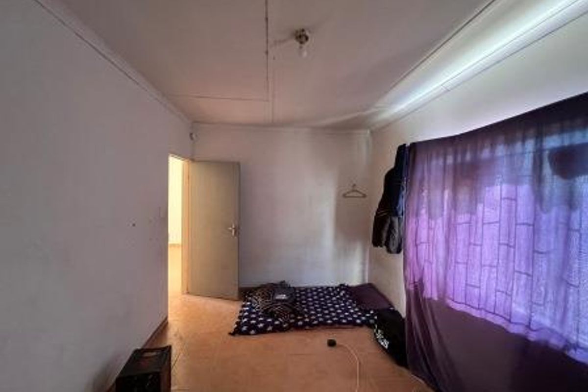 A bedroom featuring tiled flooring and ceiling light fixture, currently showing signs of wear on the walls and ceiling.