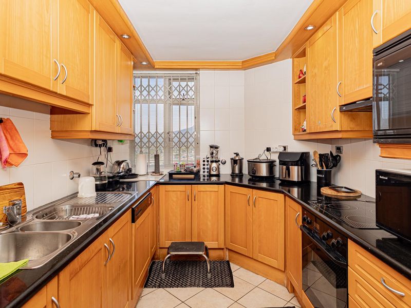 A functional kitchen featuring wooden cabinetry, black granite countertops, integrated appliances including an oven and hob, and a tiled backsplash.