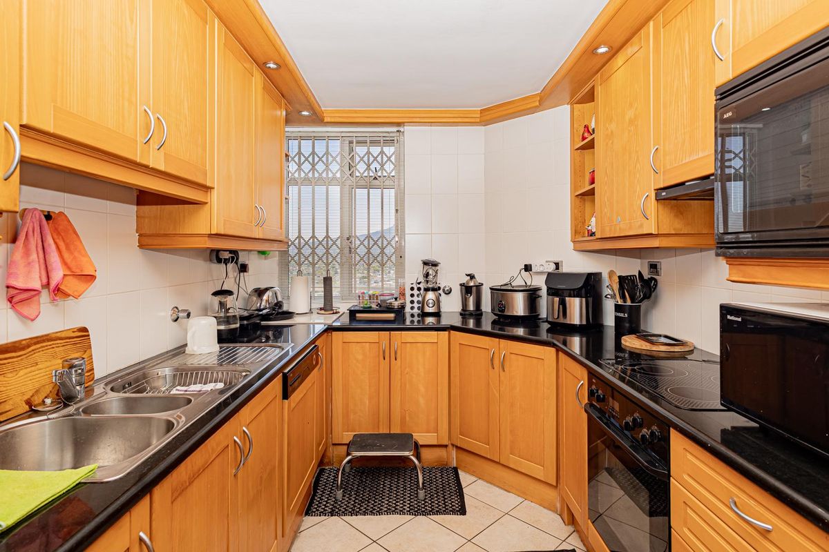 A functional kitchen featuring wooden cabinetry, black granite countertops, integrated appliances including an oven and hob, and a tiled backsplash.