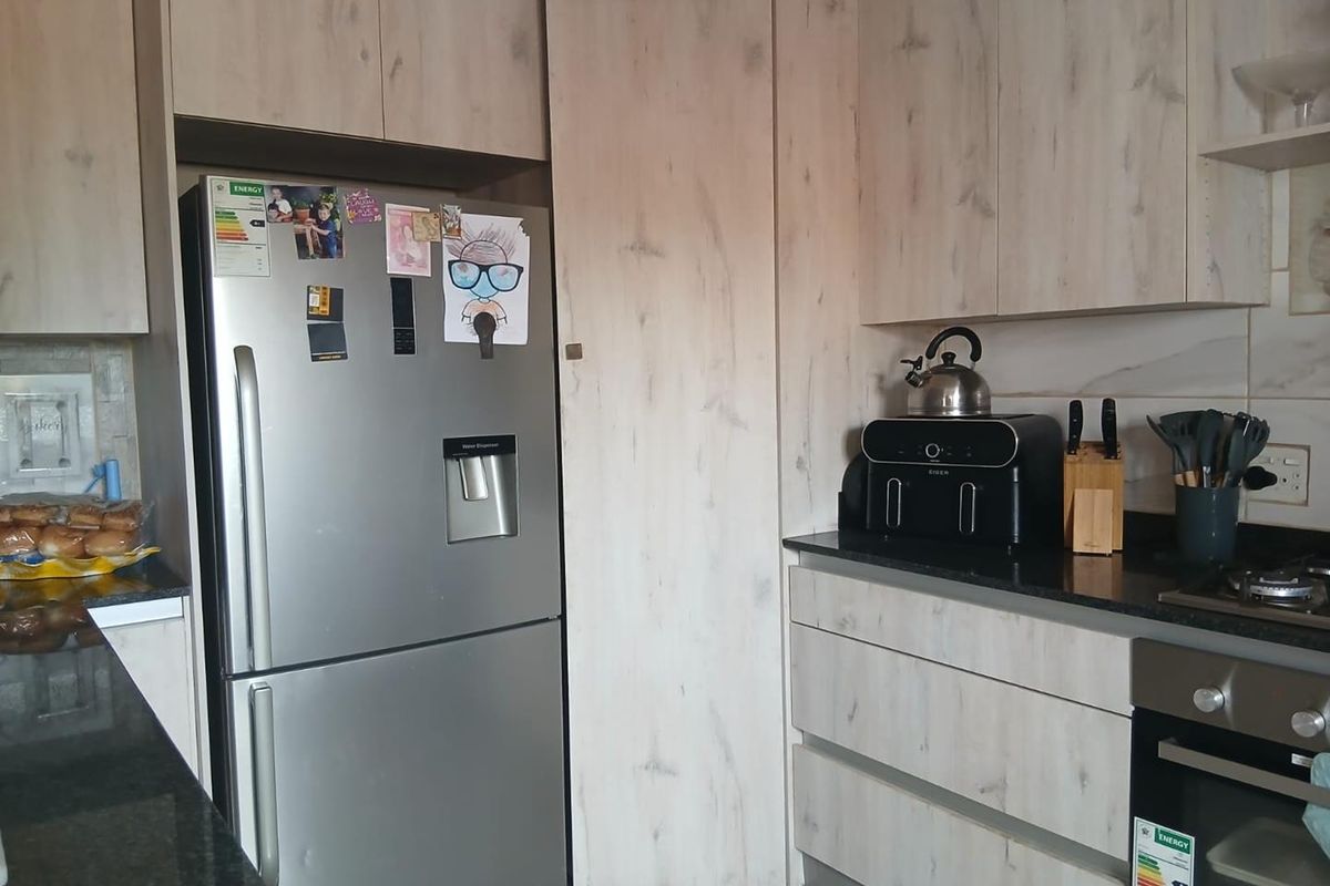 Modern kitchen featuring light wood-grain cabinetry, dark granite countertops, built-in oven, and gas hob.