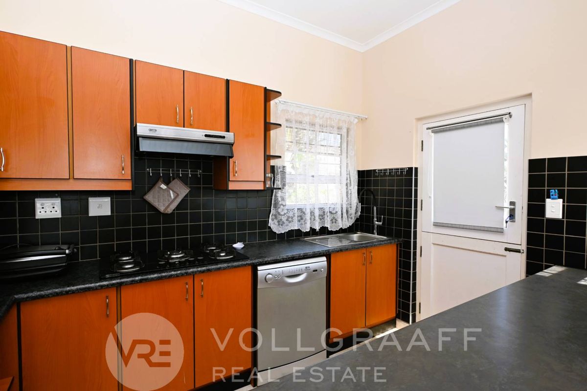A functional kitchen featuring wooden cabinetry, black tiled splashbacks, a built-in gas hob, extractor fan, and direct access to the exterior.