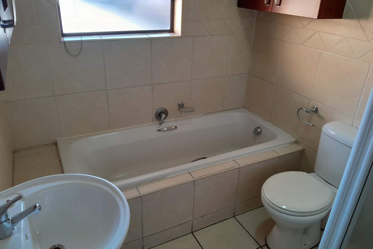 A functional bathroom featuring a built-in bathtub, pedestal basin, and toilet with neutral wall and floor tiling.