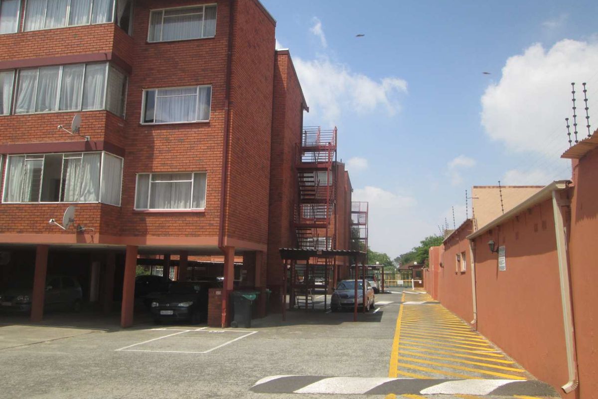 Exterior view of a multi-story brick apartment complex featuring covered parking bays, external staircases, and perimeter security fencing.