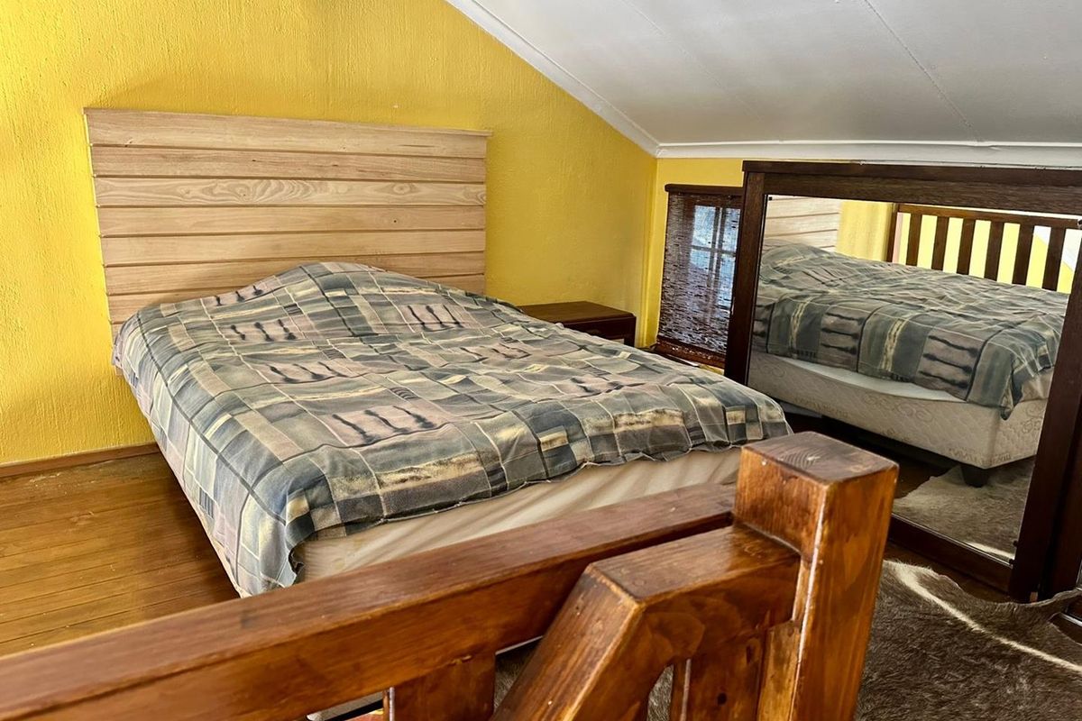 A loft-style bedroom featuring a sloped ceiling, timber flooring, and a built-in wooden headboard, providing a cozy and functional sleeping space.