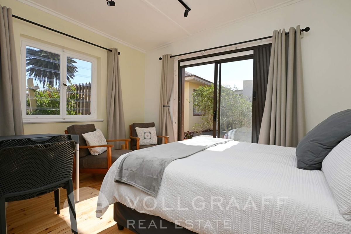 A bright bedroom featuring timber flooring, large windows, and sliding glass doors providing direct access to the outdoor area.