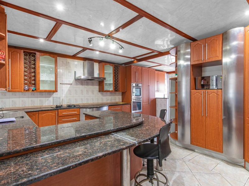 Spacious kitchen featuring granite countertops, extensive wooden cabinetry, built-in appliances, and a distinctive coffered ceiling with integrated lighting.