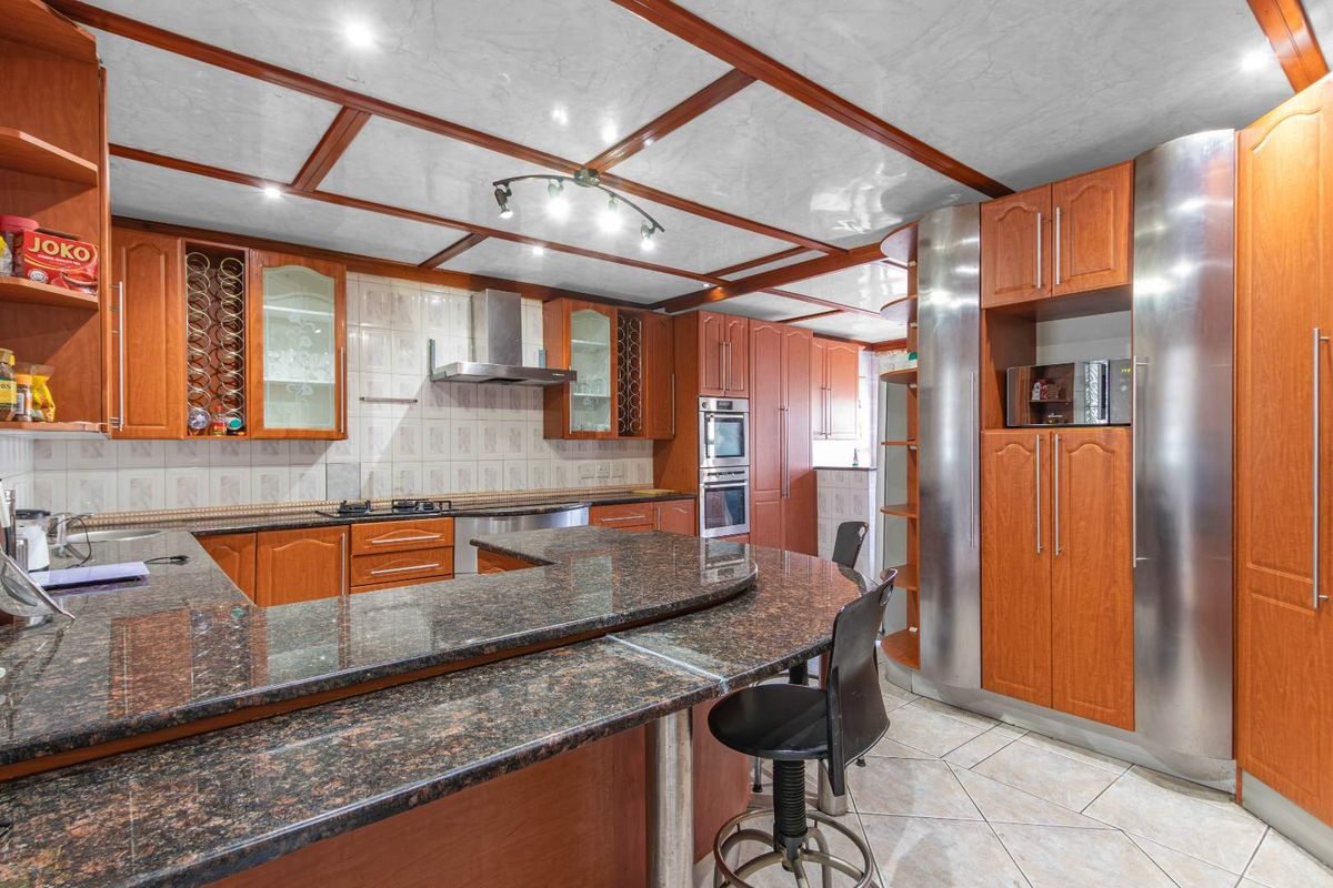 Spacious kitchen featuring granite countertops, extensive wooden cabinetry, built-in appliances, and a distinctive coffered ceiling with integrated lighting.