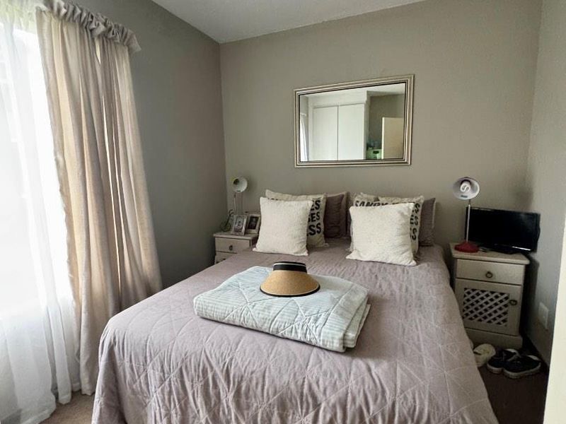 A cozy bedroom featuring neutral wall tones, carpeted flooring, and window treatments, providing a comfortable and functional sleeping space.