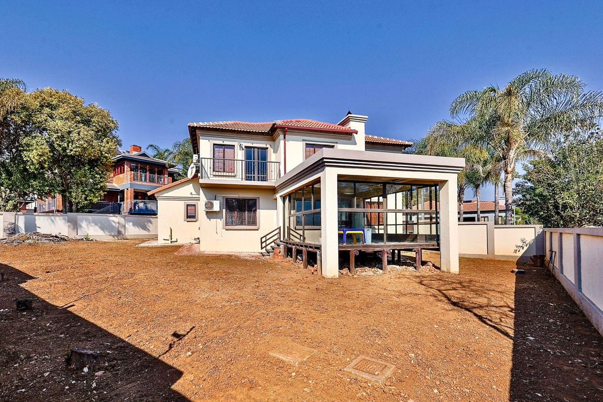 Rear view of the house featuring an enclosed patio, upper-level balcony, and a large, undeveloped garden space enclosed by perimeter walls.