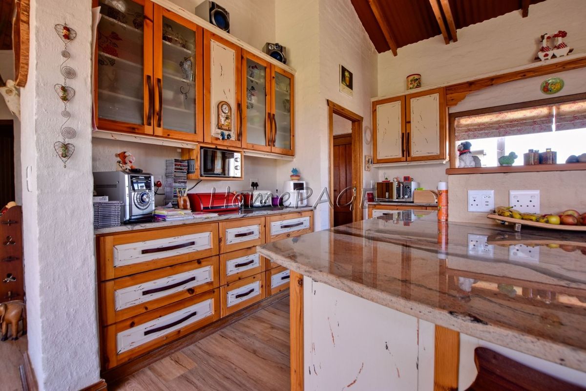A rustic-style kitchen featuring granite countertops, extensive wooden cabinetry with a distressed paint finish, and exposed timber ceiling beams.