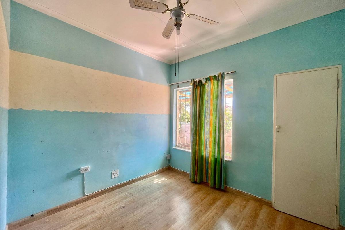 A bedroom featuring laminate flooring, a ceiling fan, and a window with natural light. The room requires cosmetic updates to the wall finishes.