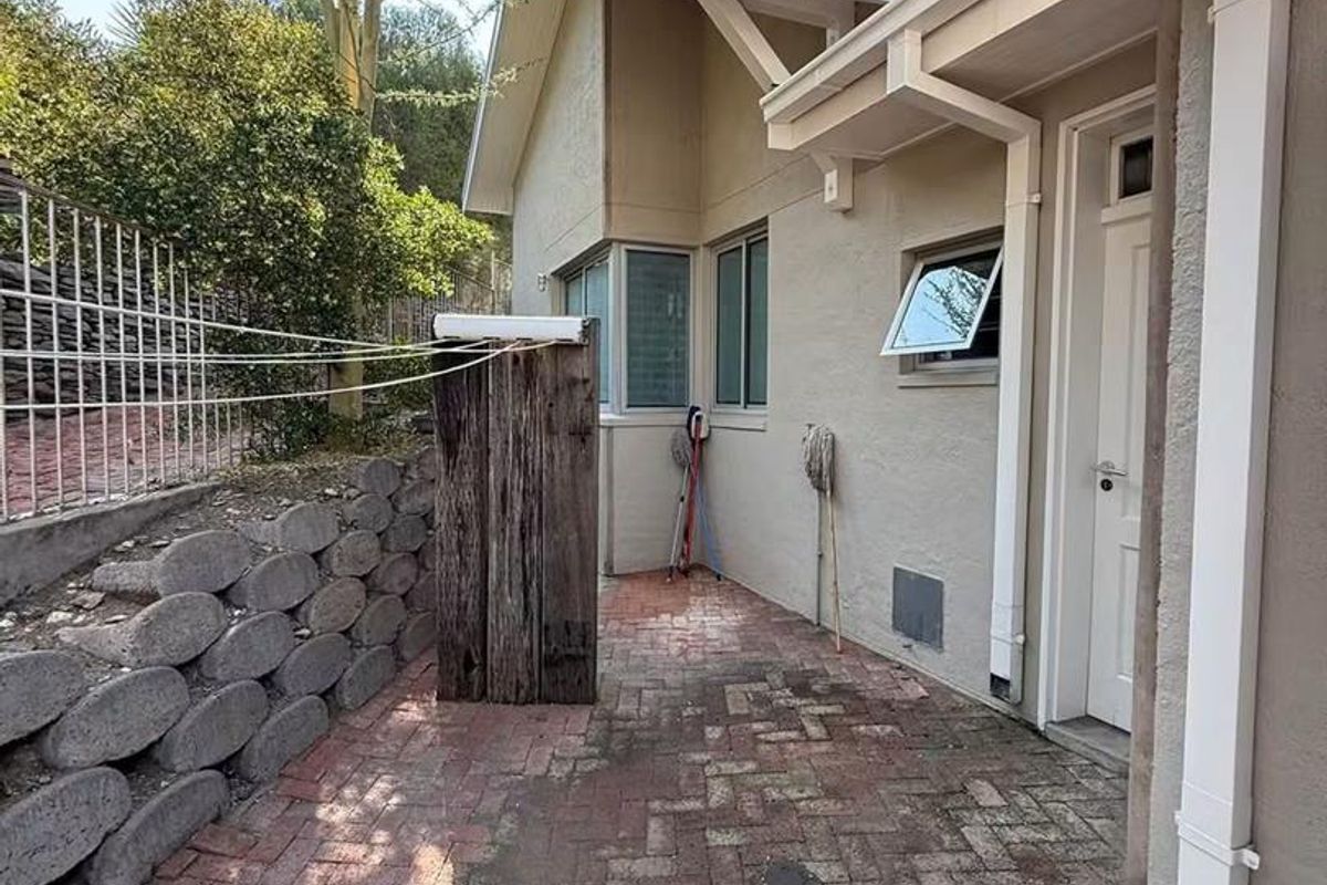 A rear exterior view featuring brick paving, a retaining wall, and access to the home via an external door.