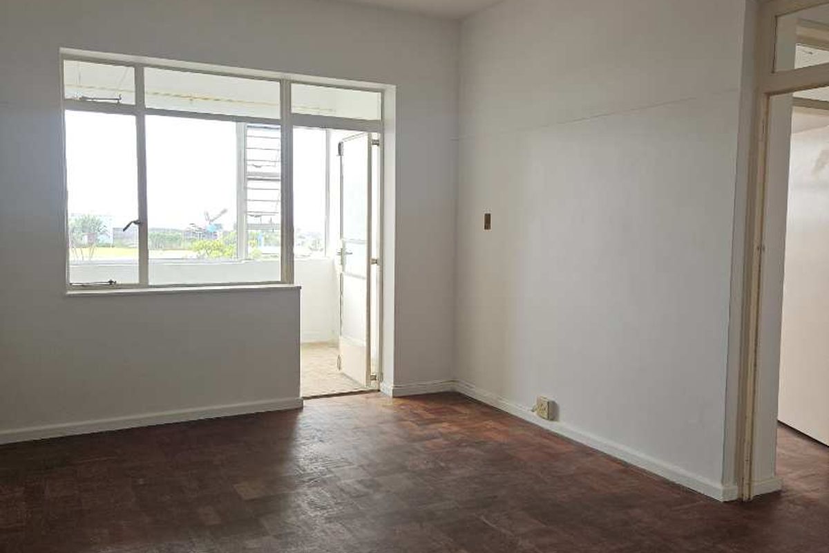 An empty living room featuring original parquet flooring, neutral walls, and access to an adjoining balcony through a glass door.