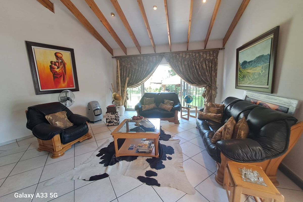 Spacious living room featuring vaulted ceilings with exposed timber beams, tiled flooring, and large sliding glass doors providing access to the outdoor area.