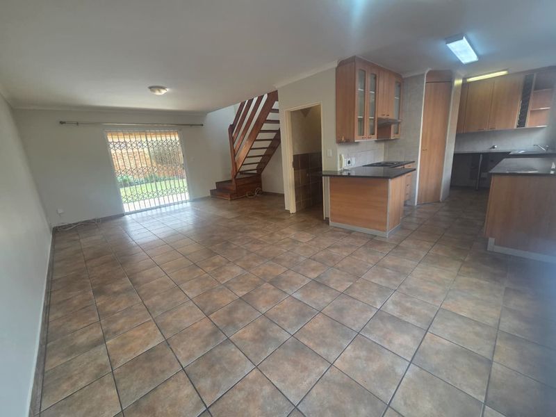 Spacious open-plan living area featuring tiled floors, a wooden staircase, and a functional kitchen with granite countertops and ample cabinetry.