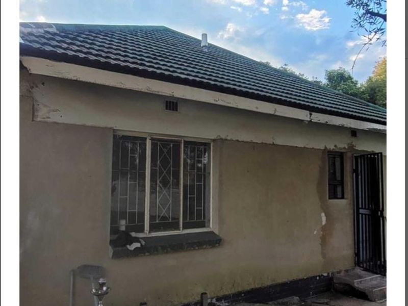 Rear exterior view of the cottage showing tiled roofing, security bars on windows, and concrete paving in need of maintenance and exterior painting.