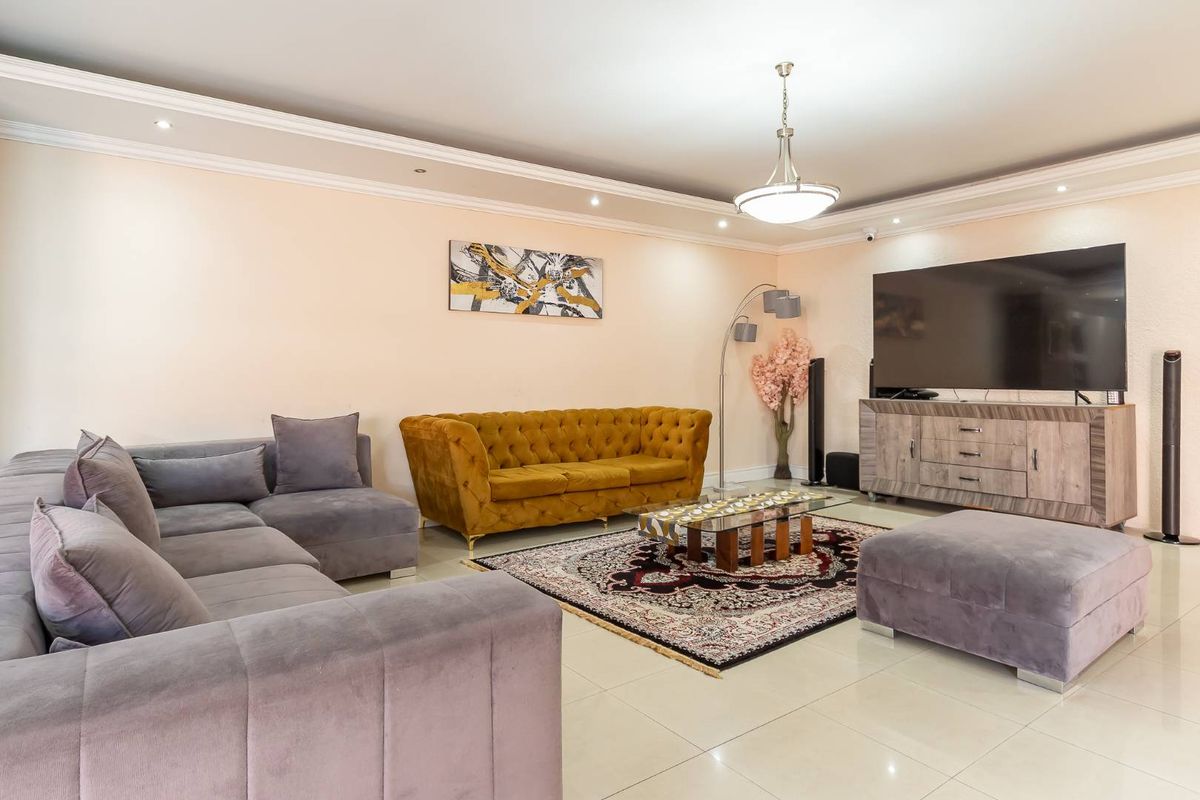 Spacious living room featuring neutral tiled flooring, crown molding, and recessed ceiling lighting, creating a comfortable and well-maintained living space.