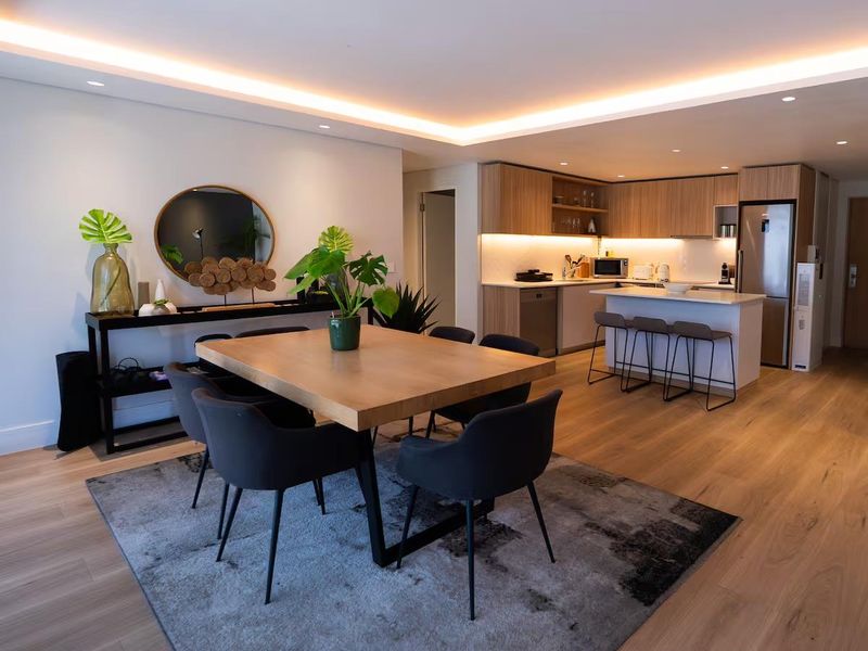 Modern open-plan living and dining area featuring high-quality timber flooring, recessed cove lighting, and a contemporary kitchen with stone countertops and integrated appliances.