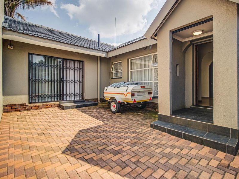 A paved rear courtyard area featuring a tiled roof structure, security gates, and window security bars, providing a functional outdoor space.