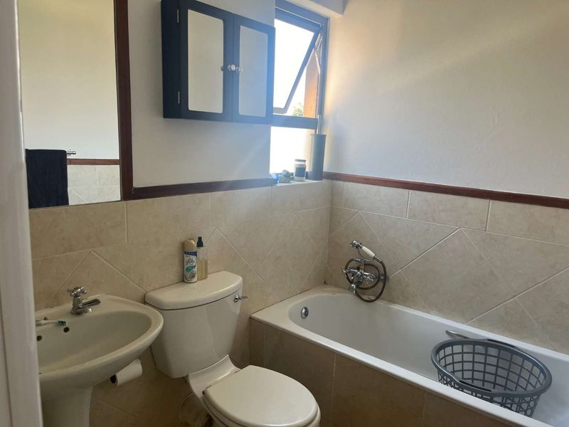 A functional bathroom featuring a pedestal basin, toilet, and bathtub with tiled splashbacks and a wall-mounted medicine cabinet.