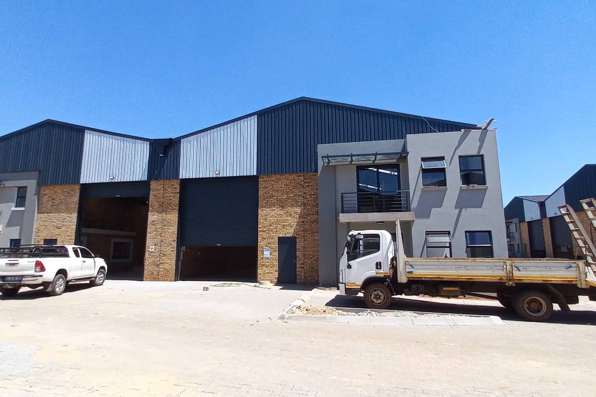 Industrial warehouse complex featuring face brick and metal cladding, large roller shutter doors, and paved exterior yard space.