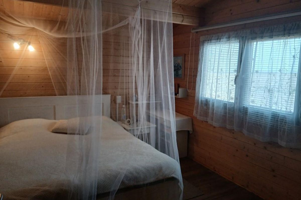 A cozy bedroom featuring natural timber wall cladding, wooden ceiling beams, and a window with integrated blinds.