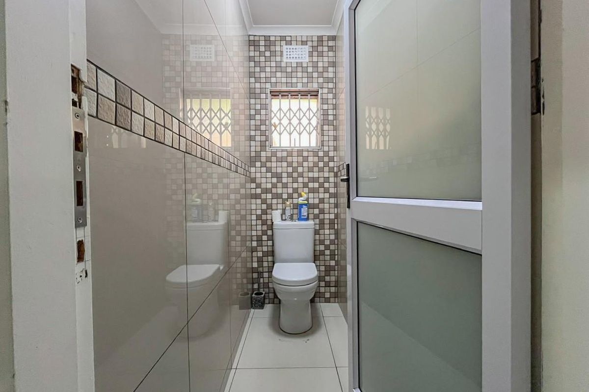 A compact bathroom featuring floor-to-ceiling tiled walls with a mosaic accent border, a white toilet, and a frosted glass door.