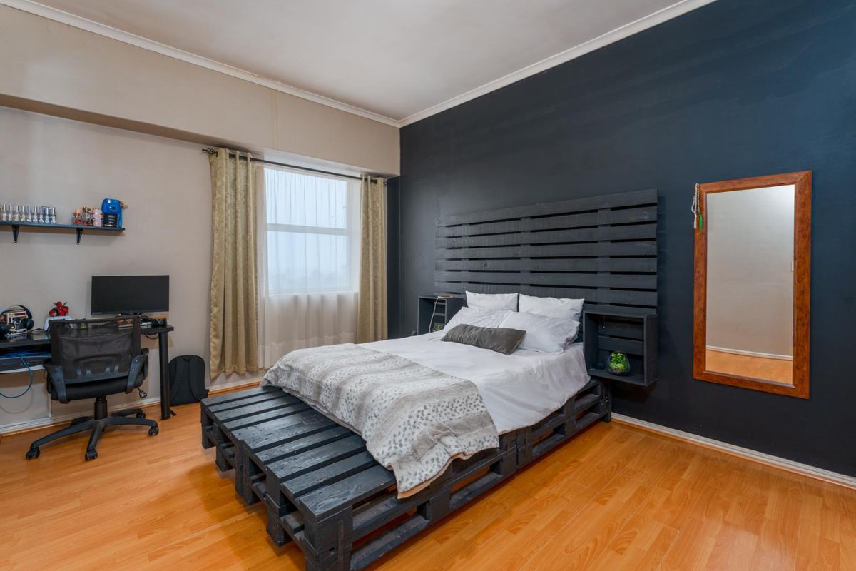 A bedroom featuring laminate flooring, a large window with curtains, and a dark accent wall.