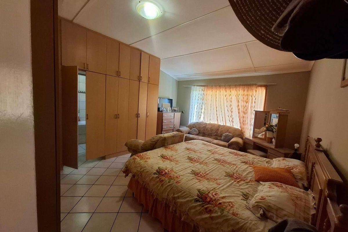 Spacious bedroom featuring tiled flooring, built-in cupboards, and natural light through a large window.