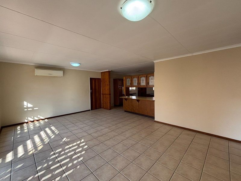 Spacious open-plan living area featuring tiled flooring, a split-system air conditioner, and a functional kitchen with built-in cabinetry and a breakfast bar.