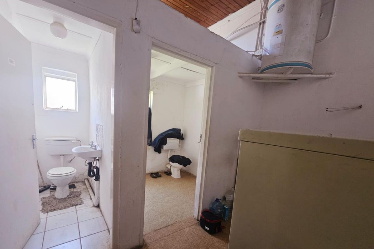 A utilitarian bathroom area featuring two separate toilet cubicles, a wall-mounted geyser, and basic sanitary fixtures in need of renovation.