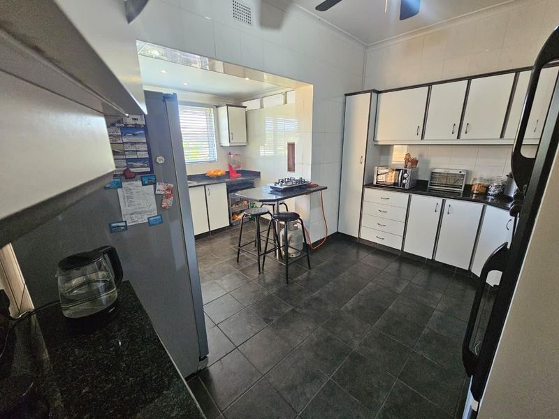 A functional kitchen featuring white cabinetry, dark granite countertops, and tiled flooring, offering a practical layout with ample storage space.