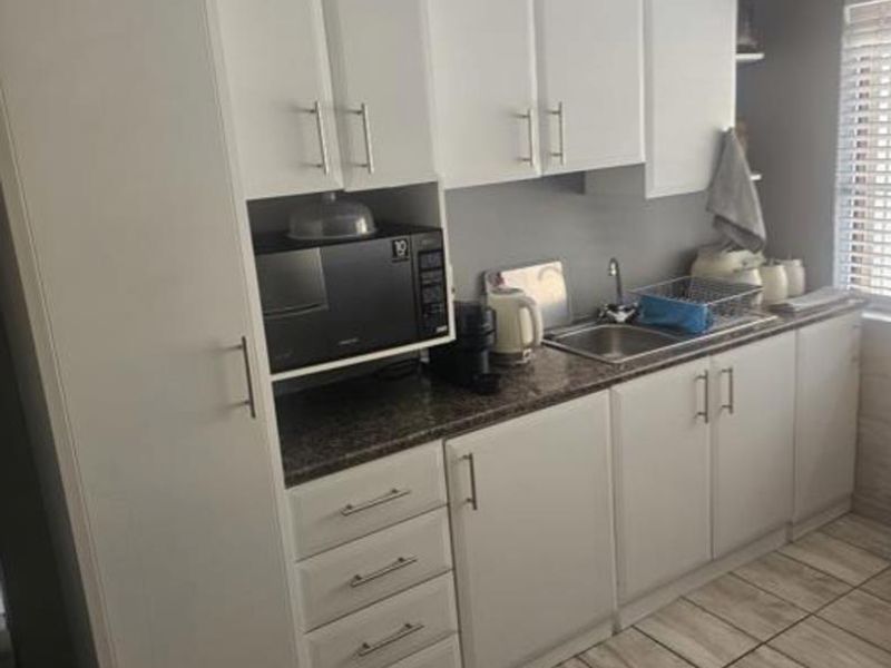 A functional kitchen featuring white cabinetry, granite-look laminate countertops, a stainless steel sink, and tiled flooring.