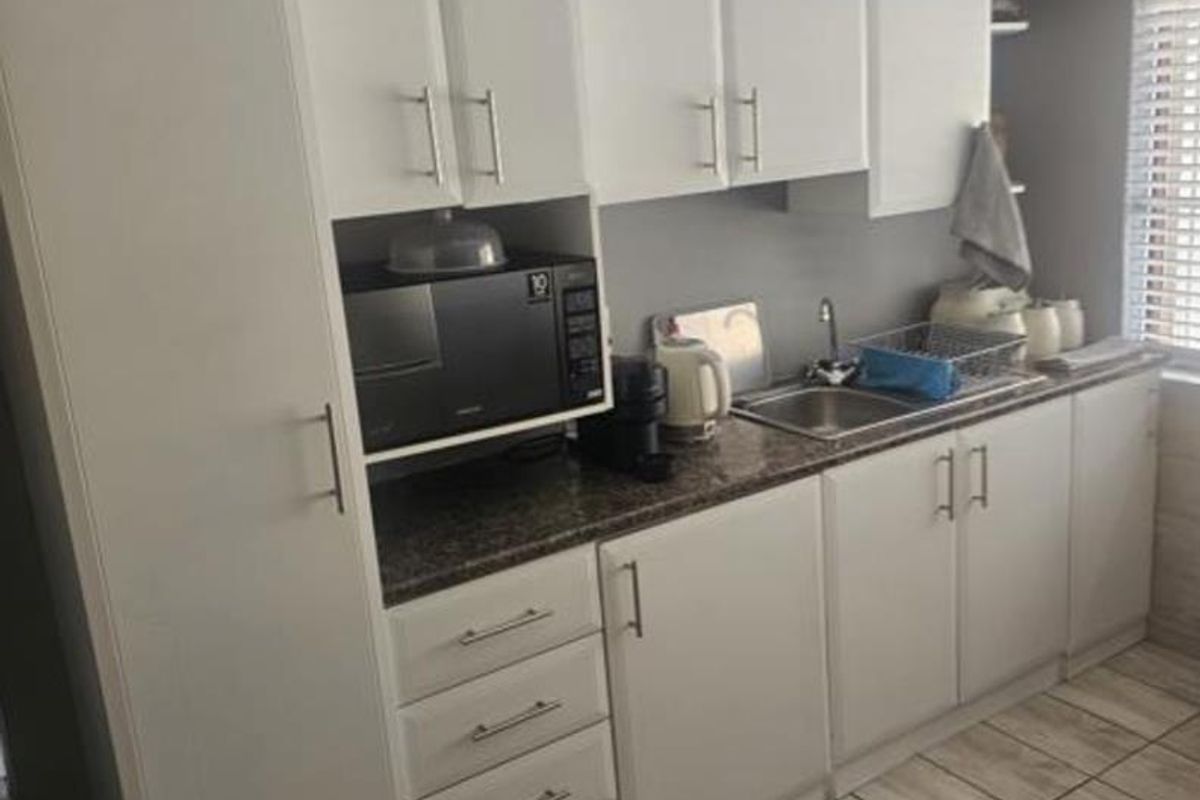 A functional kitchen featuring white cabinetry, granite-look laminate countertops, a stainless steel sink, and tiled flooring.
