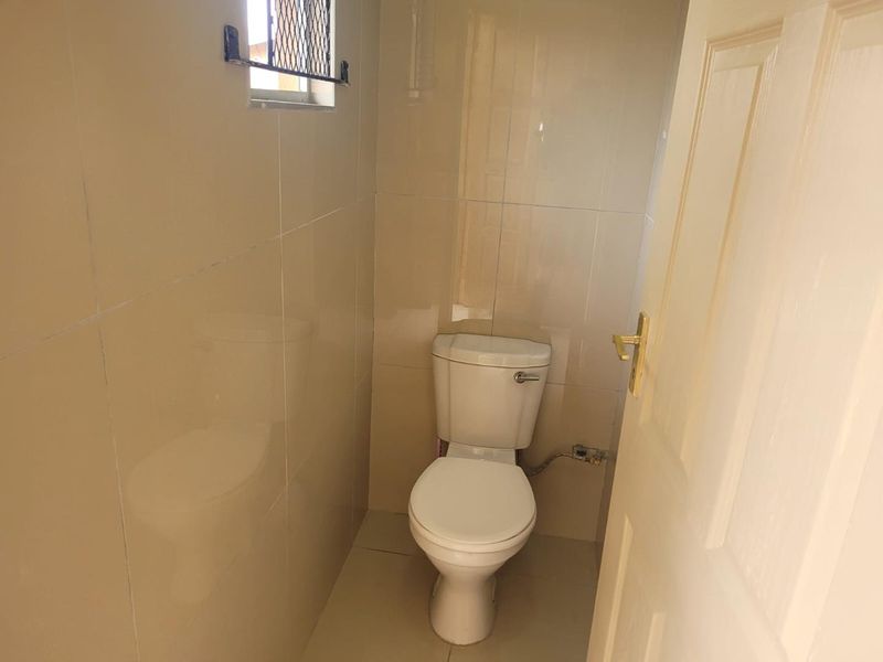 A compact guest bathroom featuring neutral ceramic wall and floor tiles and a standard toilet.