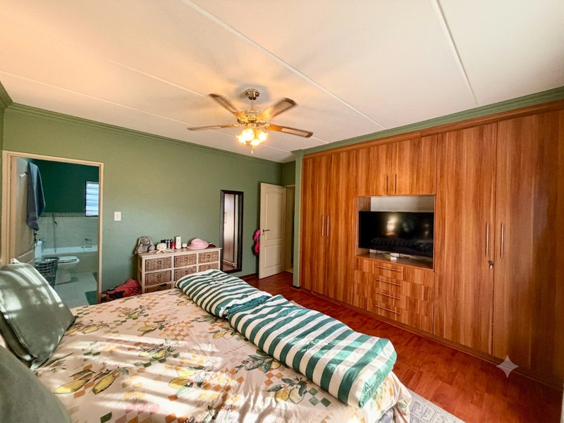 Spacious bedroom featuring extensive built-in wooden cabinetry, laminate flooring, a ceiling fan, and direct access to an en-suite bathroom.