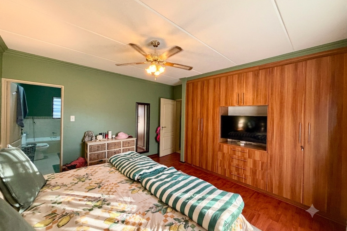 Spacious bedroom featuring extensive built-in wooden cabinetry, laminate flooring, a ceiling fan, and direct access to an en-suite bathroom.