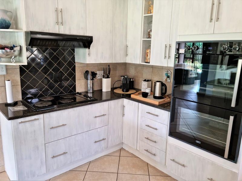 A functional kitchen featuring white cabinetry, granite countertops, a built-in double oven, electric hob, and a decorative tiled backsplash.