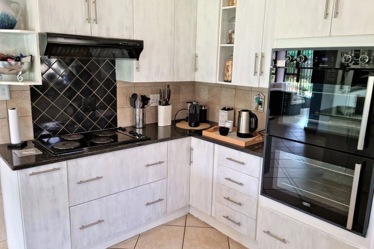 A functional kitchen featuring white cabinetry, granite countertops, a built-in double oven, electric hob, and a decorative tiled backsplash.