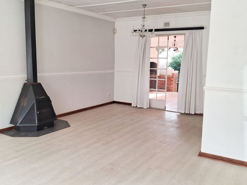 Spacious living room featuring a freestanding fireplace, neutral laminate flooring, and direct access to an outdoor patio area through glass panel doors.
