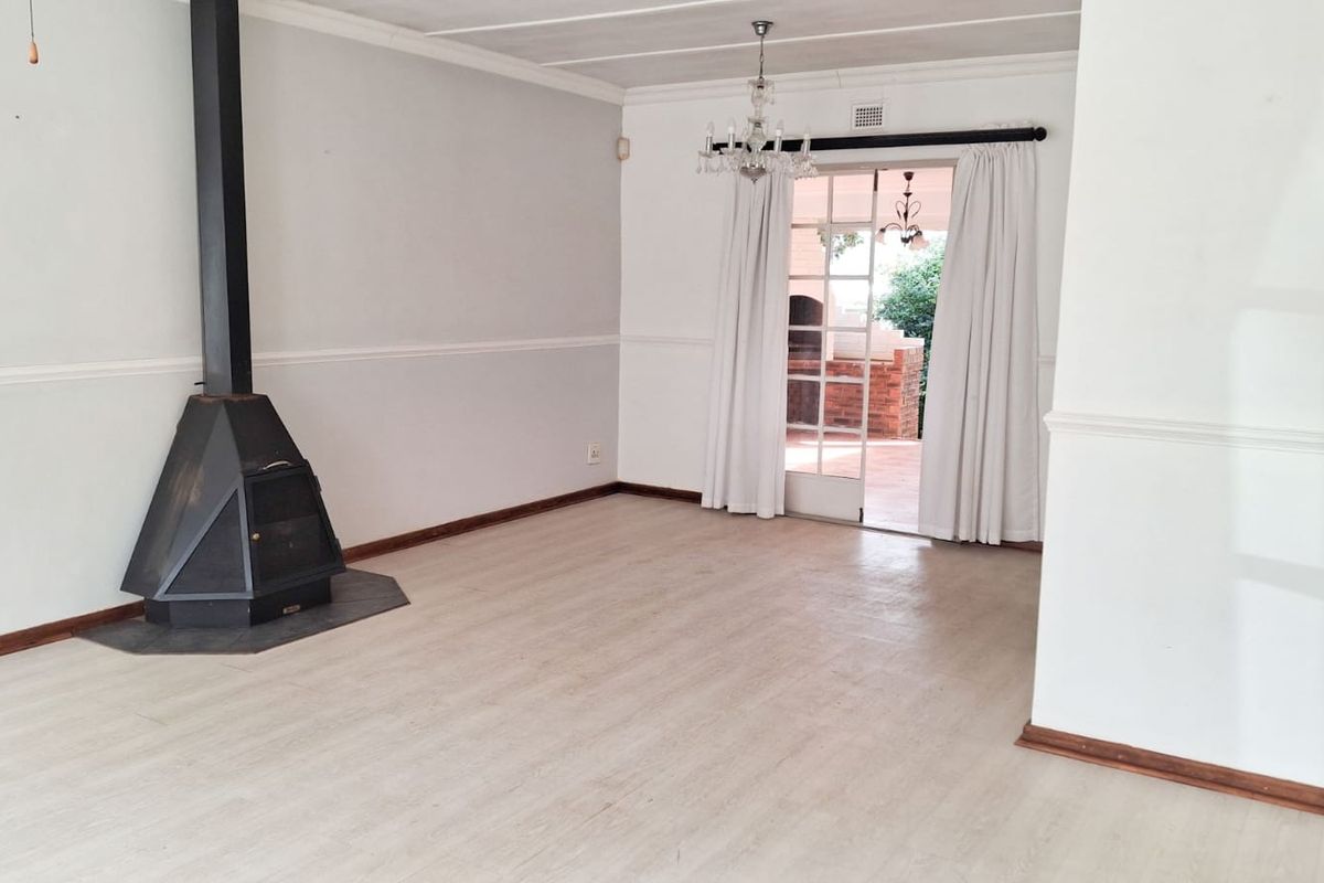 Spacious living room featuring a freestanding fireplace, neutral laminate flooring, and direct access to an outdoor patio area through glass panel doors.