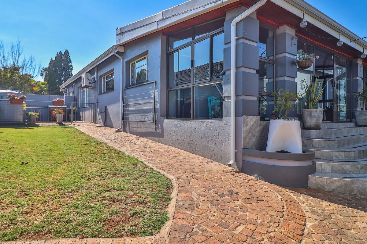 Rear exterior view featuring a paved walkway, tiled patio steps, and well-maintained garden area with aluminium window frames.