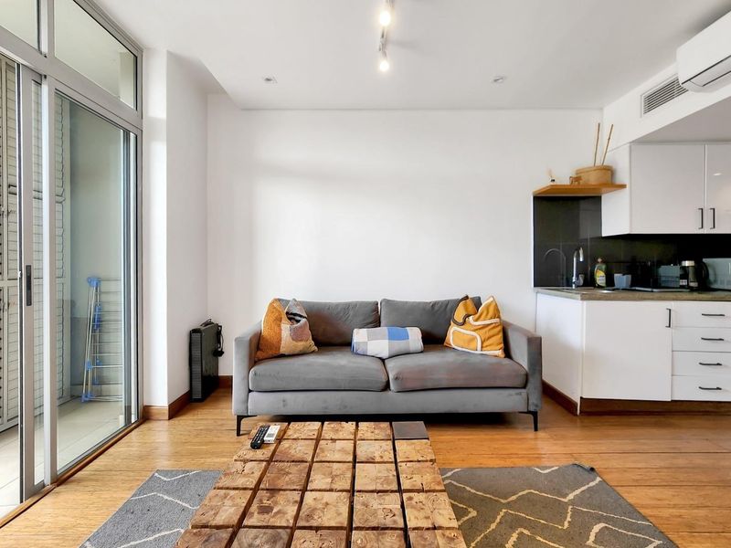 A bright open-plan living area featuring hardwood flooring, modern kitchen cabinetry, and a large sliding glass door leading to a private balcony.