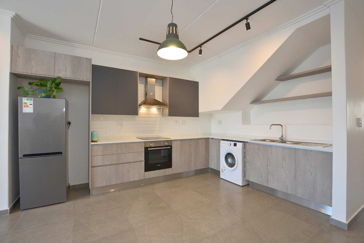 Modern kitchen featuring two-tone cabinetry, subway tile backsplash, integrated appliances, and sleek tiled flooring under a sloped ceiling with track lighting.
