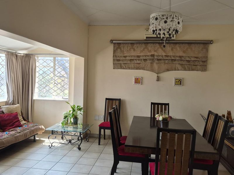 Open-plan living and dining area featuring tiled flooring, security-barred windows, and a wall-mounted air conditioning unit.
