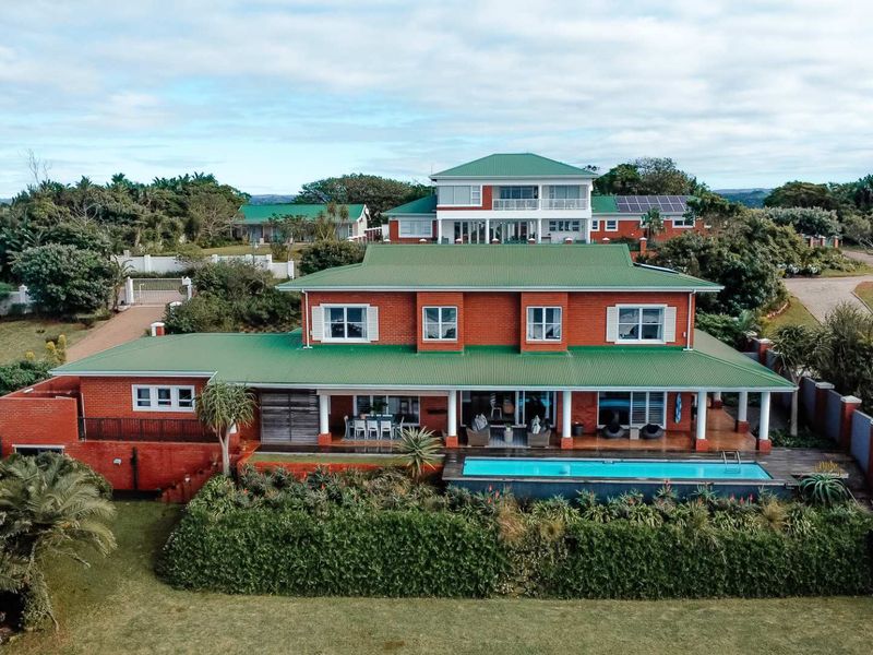 Aerial view of a spacious red brick house featuring a green metal roof, a swimming pool, and a covered patio area.
