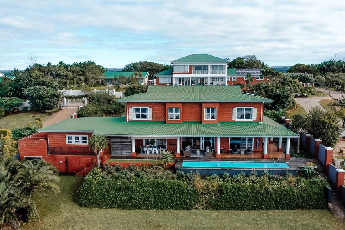 Aerial view of a spacious red brick house featuring a green metal roof, a swimming pool, and a covered patio area.
